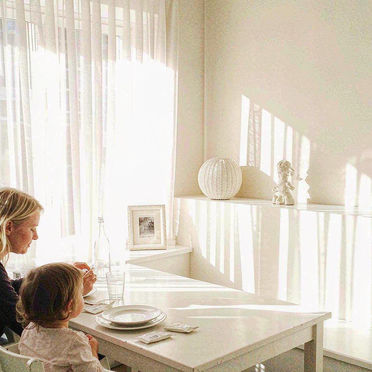 Caucasian mother and child sharing a calm morning moment at a bright white breakfast table with soft window light