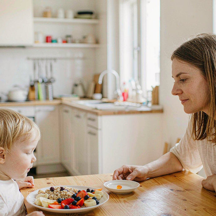 Caucasian mother and child sharing a bright breakfast table with a small amber gummy on a ceramic dish
