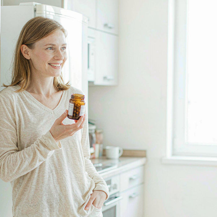 Smiling woman in a bright morning kitchen holding a jar of heart-health gummies, first month of use
