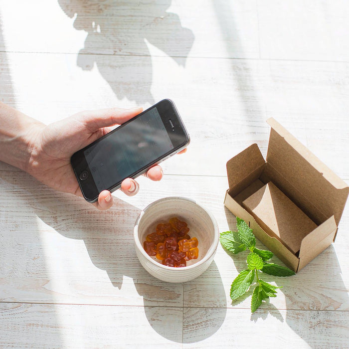 Overhead flat-lay of kid gummy vitamins and a parcel on a sunlit oak counter held by a fair-skinned hand
