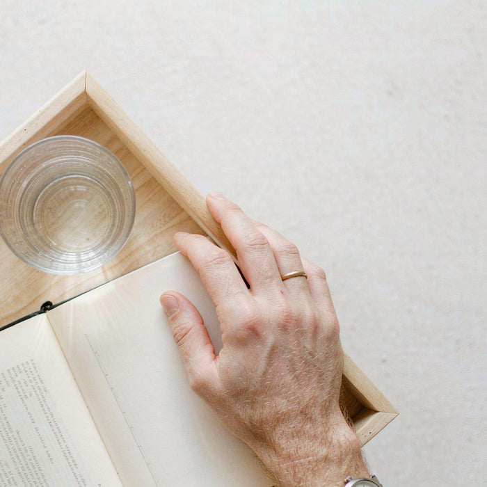 Overhead flat-lay of a light wooden tray with a fair light skin hand near a wellness notebook and a glass of water.