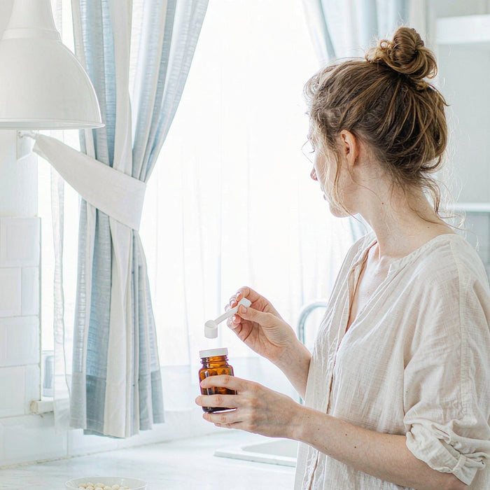 Woman with fair skin holding an amber jar of plant-based gummy supplements in a bright morning kitchen