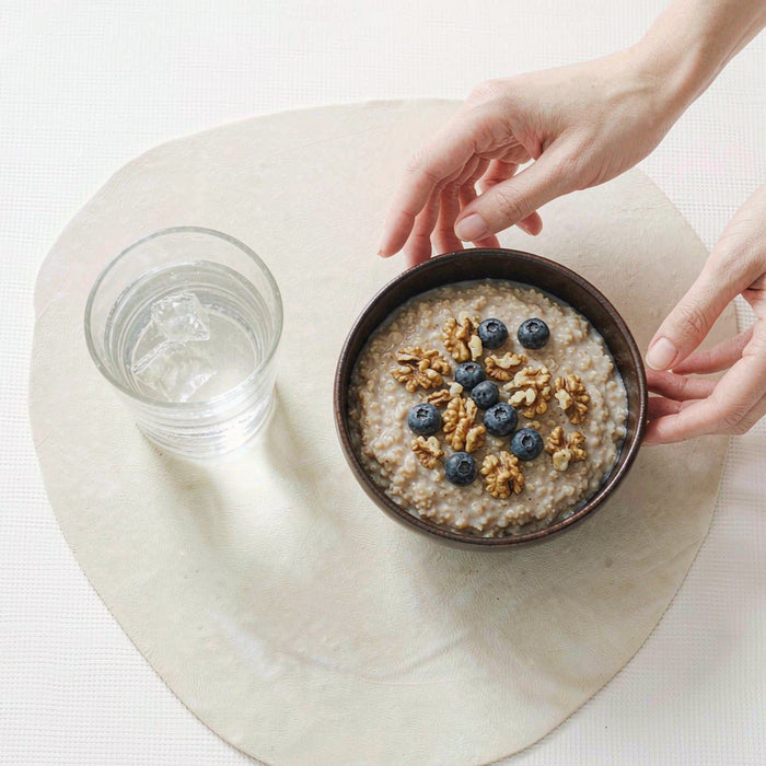 Overhead breakfast table with walnuts, blueberries and oatmeal beside water, soft morning light