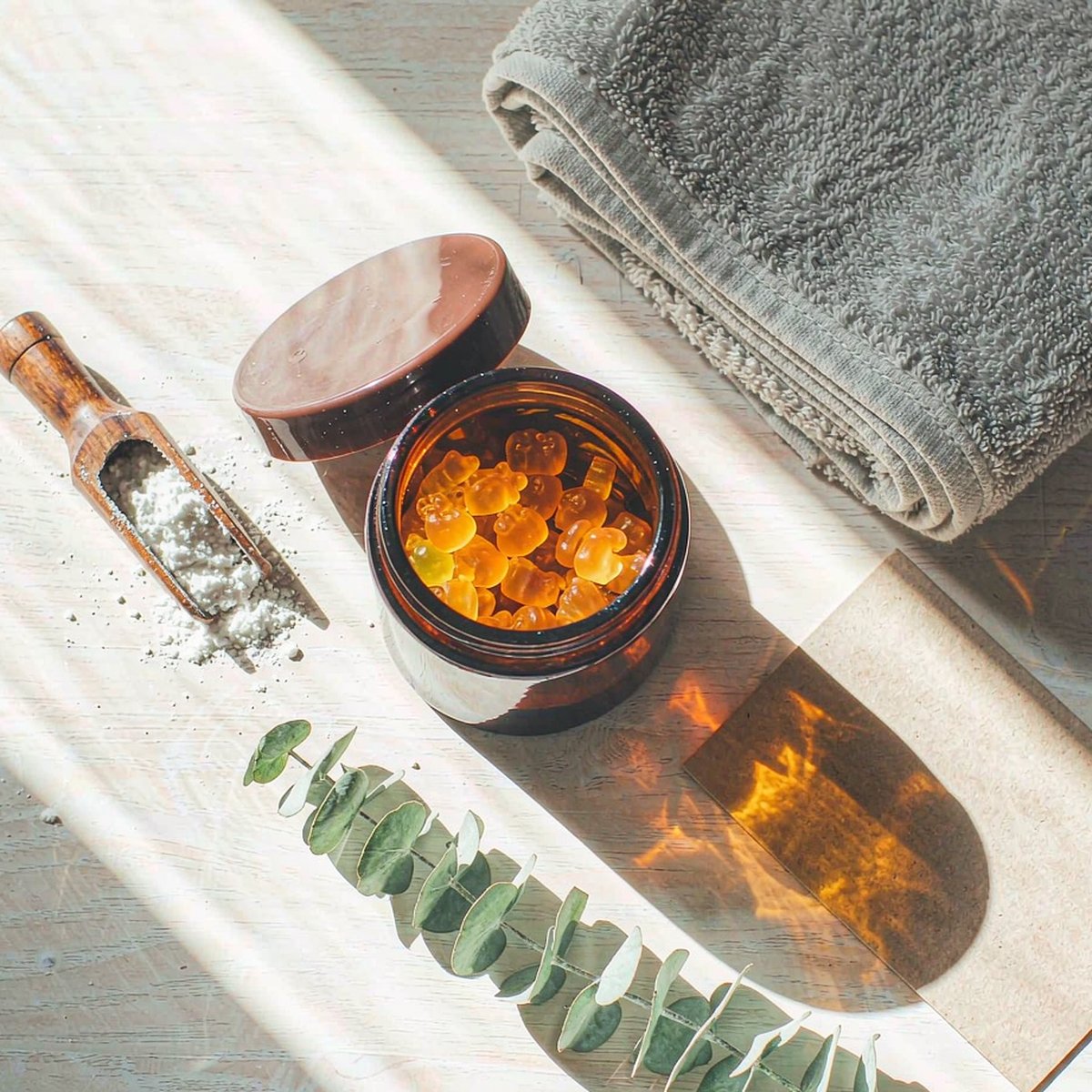 Overhead flat-lay of an amber gummy jar, amino acid powder and gym towel on a light oak morning table