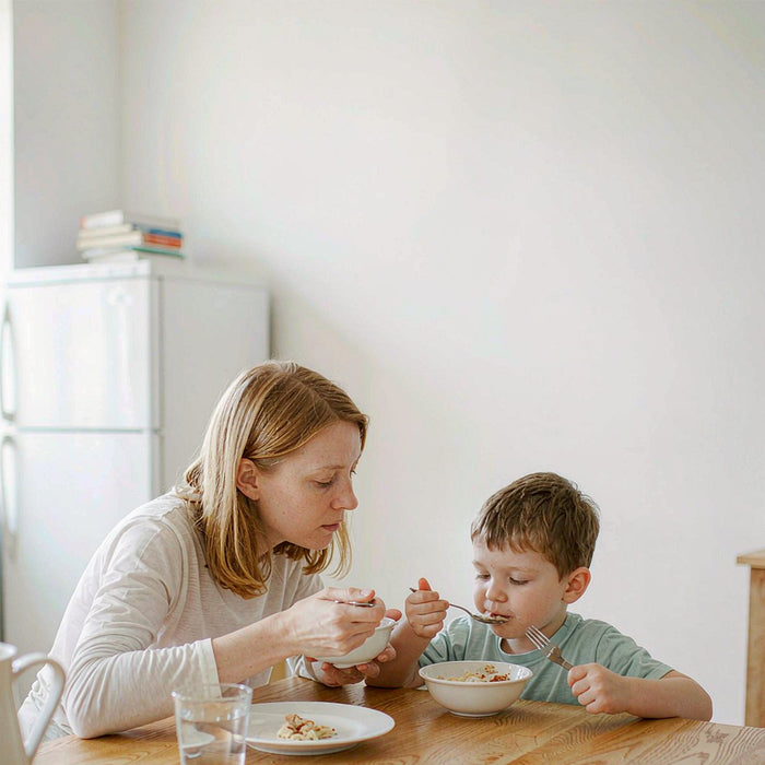 A Caucasian mother and her young son share a calm morning wellness routine at a sunlit oak breakfast table in an airy minimalist kitchen.