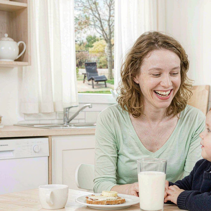 Fair-skinned mother with light brown hair smiling with her child over a bright breakfast in a sunlit kitchen