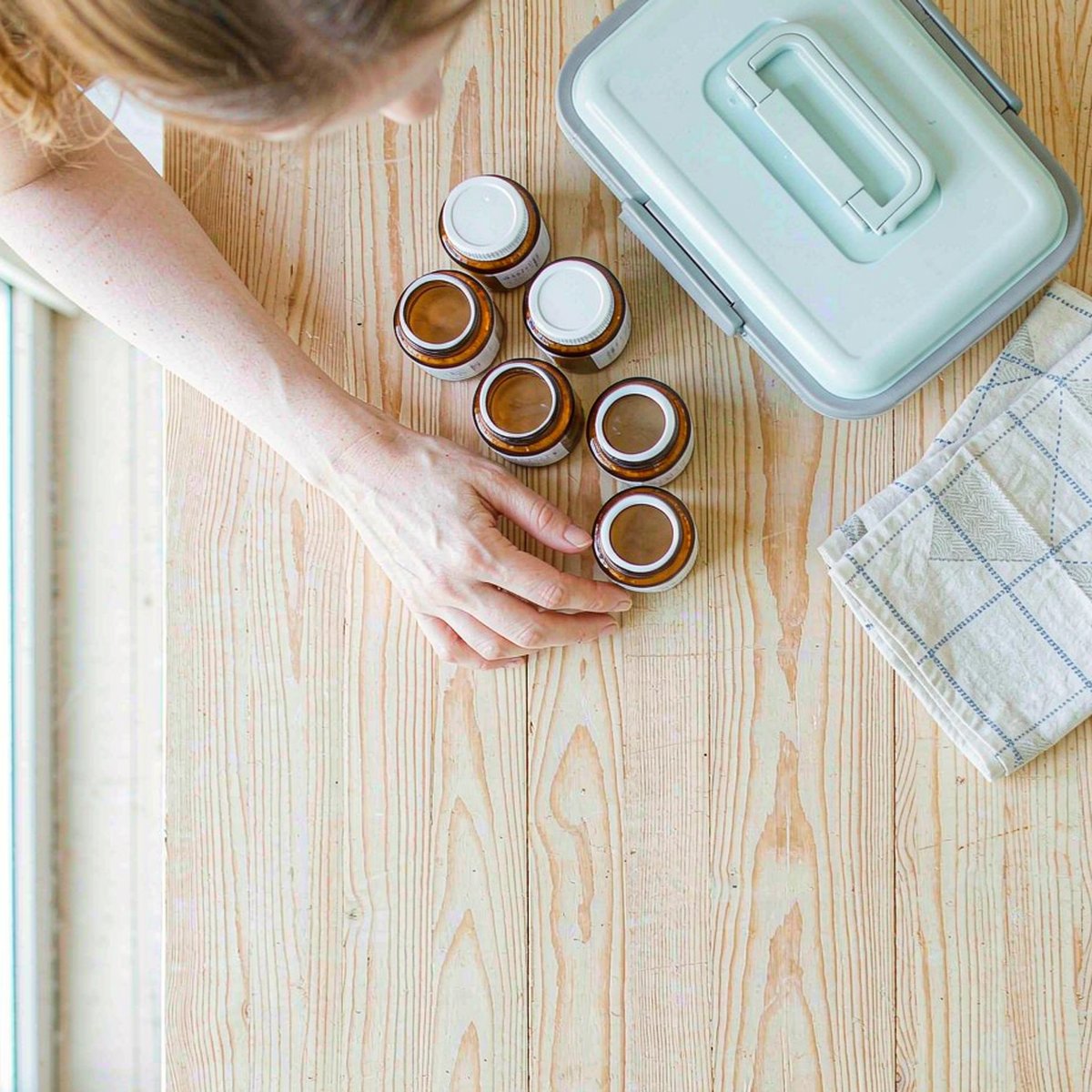 Overhead flat lay of amber supplement jars and a child's lunchbox on a sunlit maple kitchen counter, arranged by a mother's hand