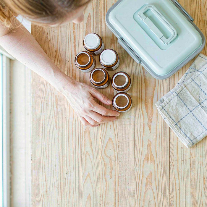 Overhead flat lay of amber supplement jars and a child's lunchbox on a sunlit maple kitchen counter, arranged by a mother's hand