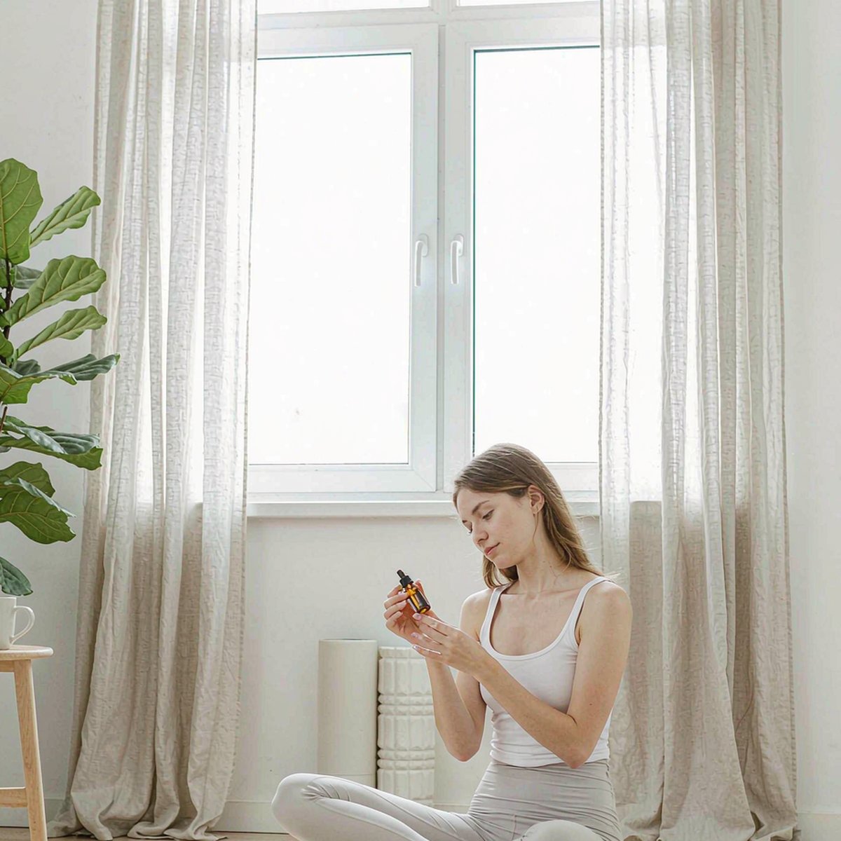 Young Western woman holding an amber dropper bottle in a bright home workout recovery corner after morning stretching