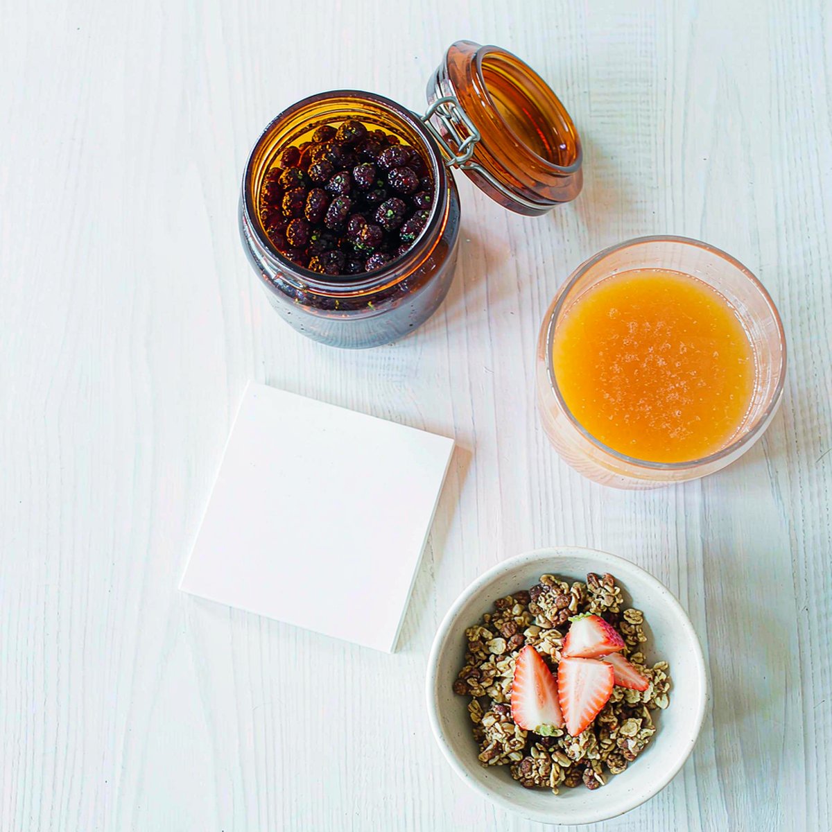 Overhead view of a morning breakfast table with an amber jar of berry gummies, orange juice and granola