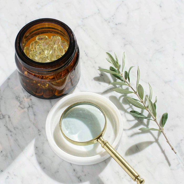 Overhead flat-lay of amber gummy jar, porcelain dish and magnifying glass on marble, quality testing