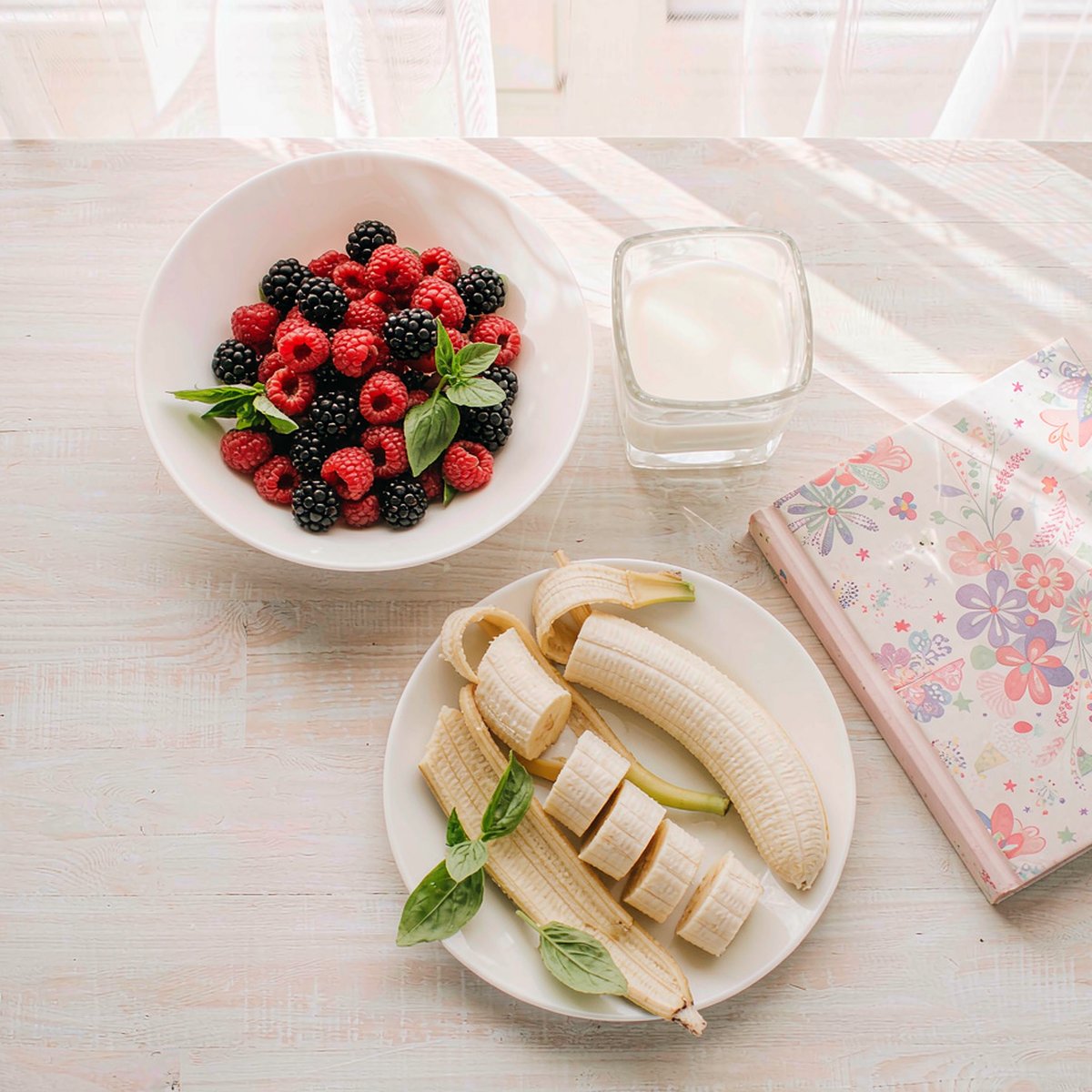 Overhead flat-lay of a wholesome kids breakfast with fresh berries, banana and milk on a pale table in soft light