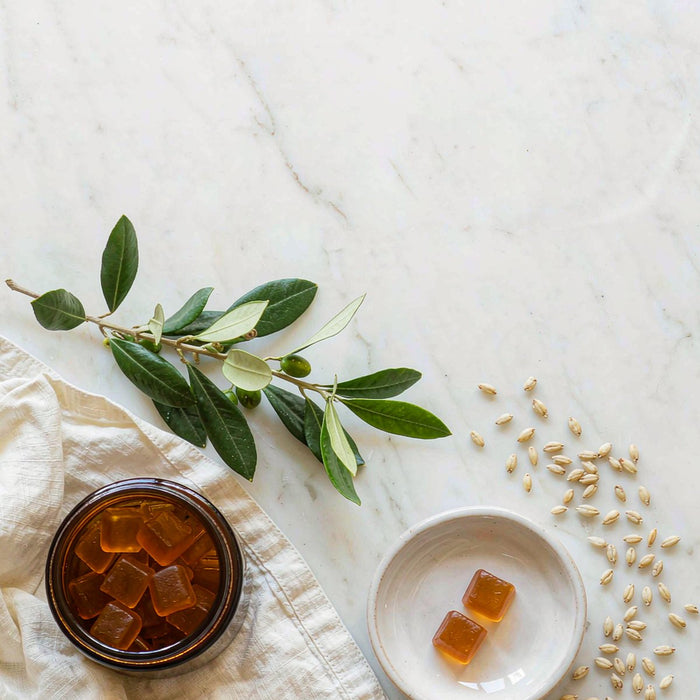 Overhead view of an amber gummy jar, ceramic dish, olive branch and oats on a white marble countertop