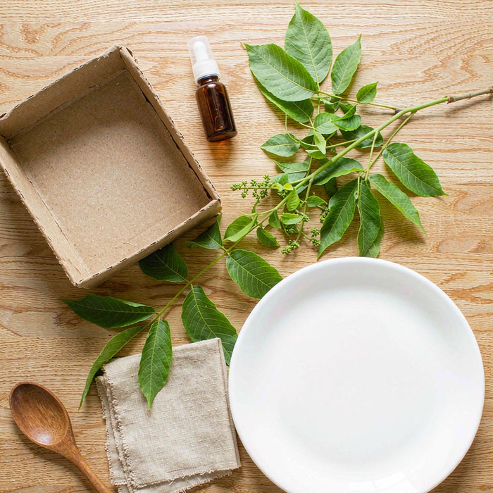 Overhead flat lay of a kraft box, amber dropper bottle, linen napkin and walnut leaves on warm oak