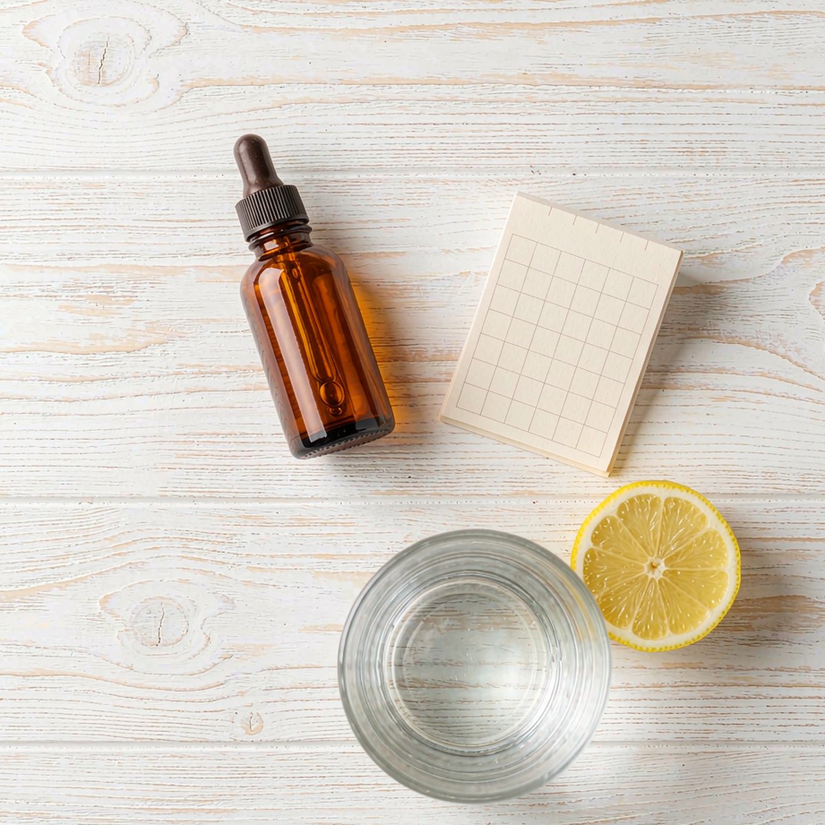 Overhead flat-lay of an amber dropper bottle with a calendar card and glass of water on an oak countertop