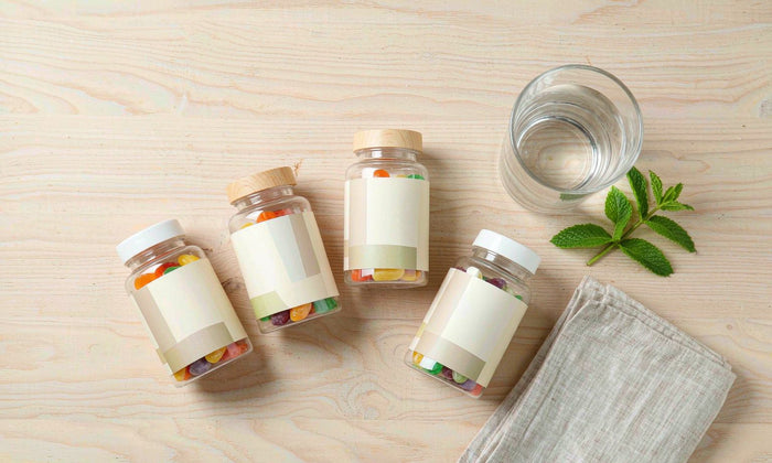 Bright minimal flat lay of q'ankyaq vegan supplement bottles and a glass of water on a light wood table