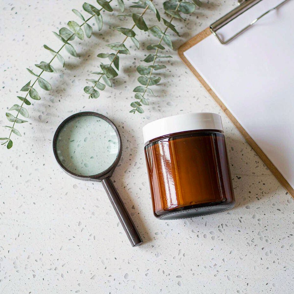Quality testing flat lay with amber jar, magnifying glass and blank certificate on white quartz