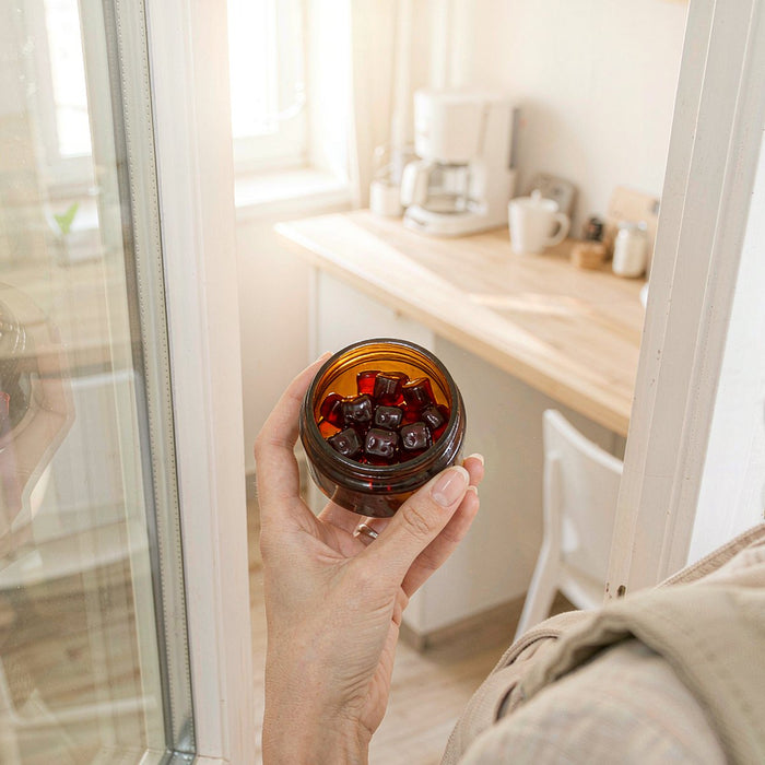 Hand holding an amber jar of berry gummies in a sunlit kitchen doorway on a busy morning