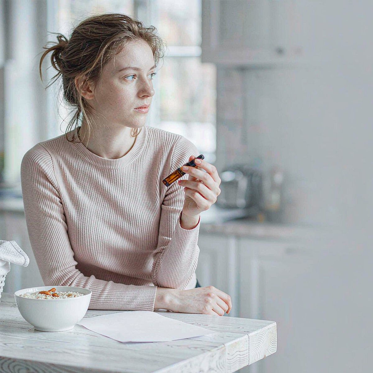 Woman holding an amber HMB and L-leucine drops bottle beside a weekly planner in a bright morning kitchen