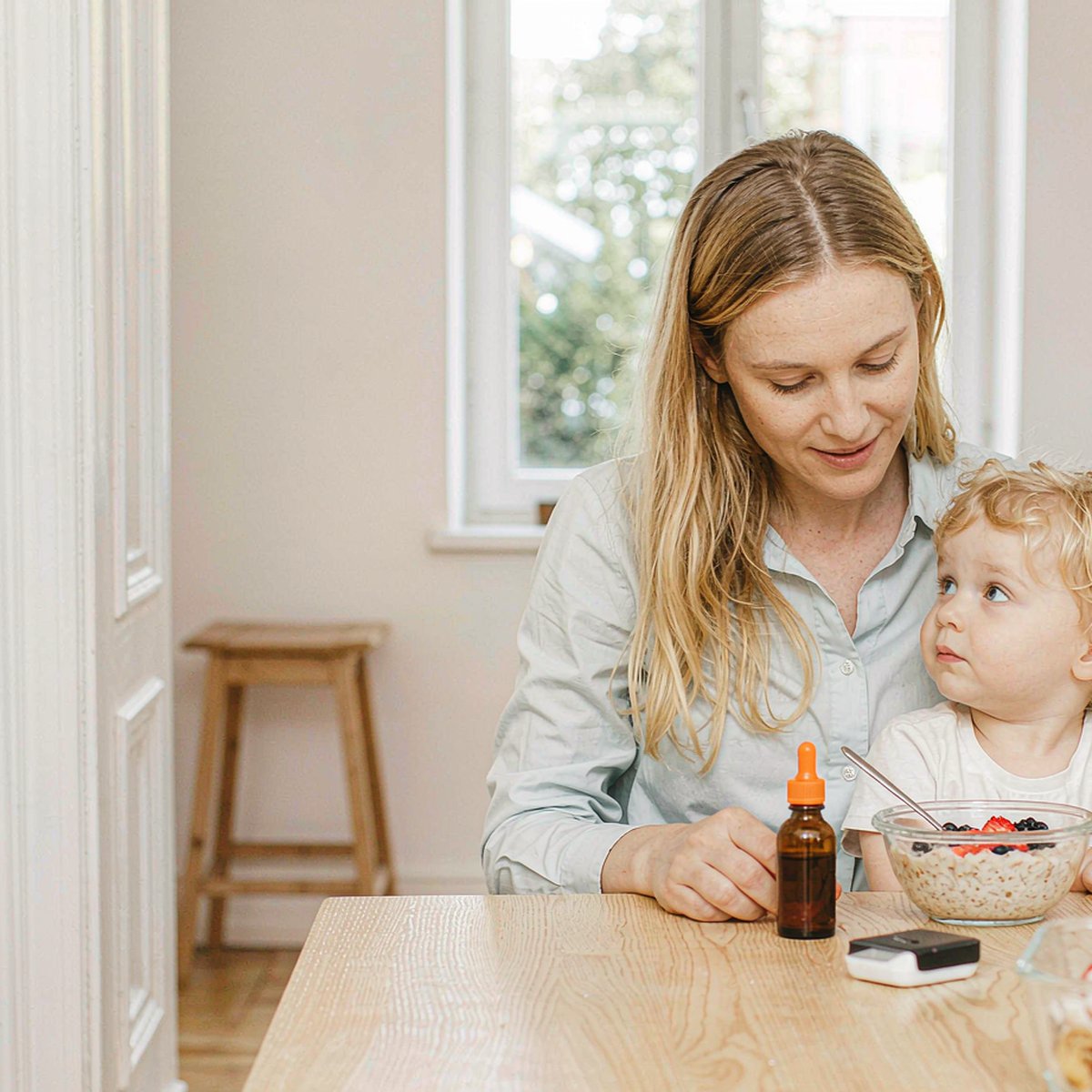 Sunlit breakfast nook where a mother and child share a morning meal beside a small amber dropper bottle