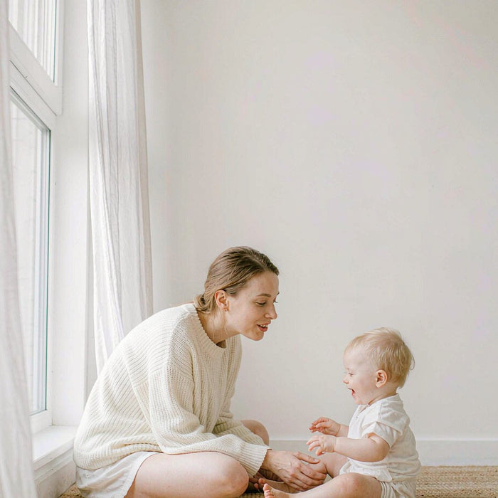 Caucasian mother with fair light skin beside a smiling toddler on a bright minimalist rug, soft daylight