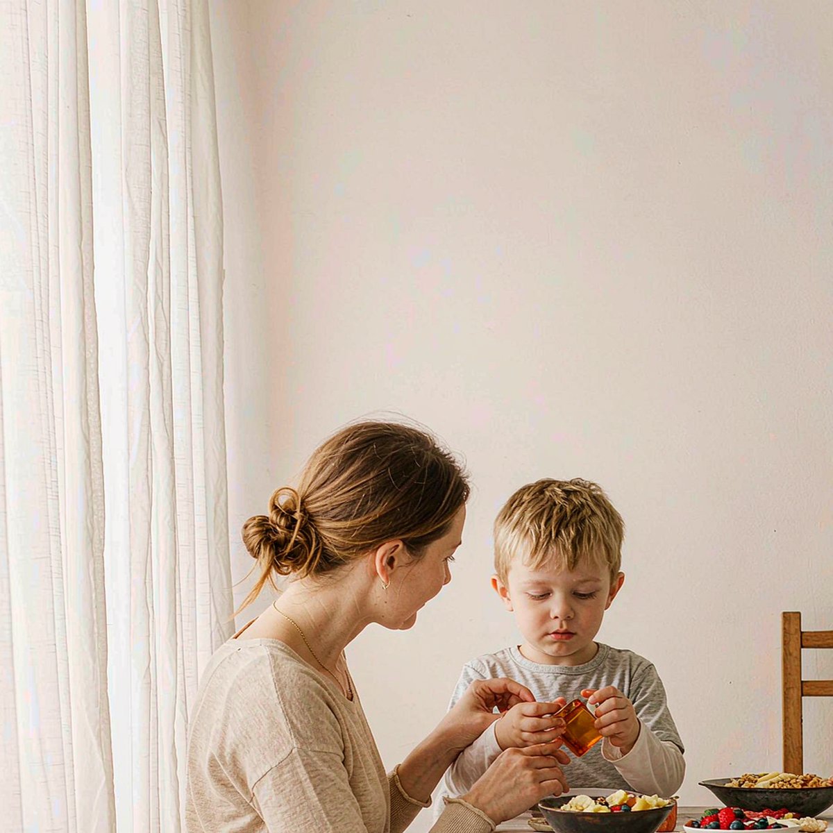 Western mother with light brown hair and her son sharing an amber gummy at a bright breakfast table with berries