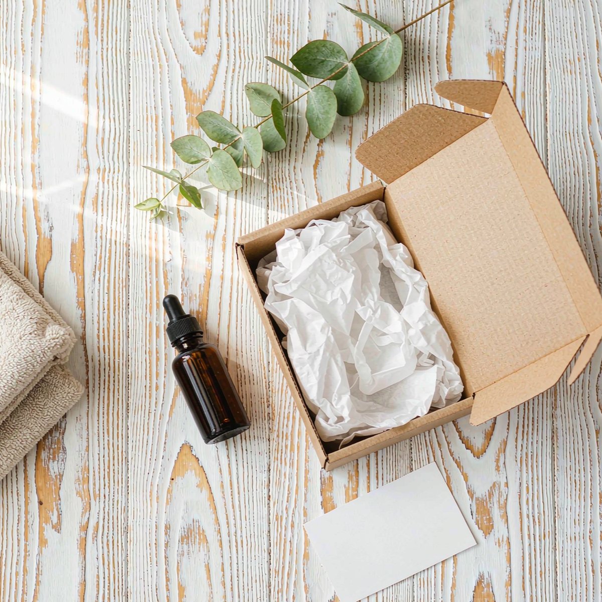 Kraft subscription box with amber dropper bottle on white oak desk, flat-lay morning scene