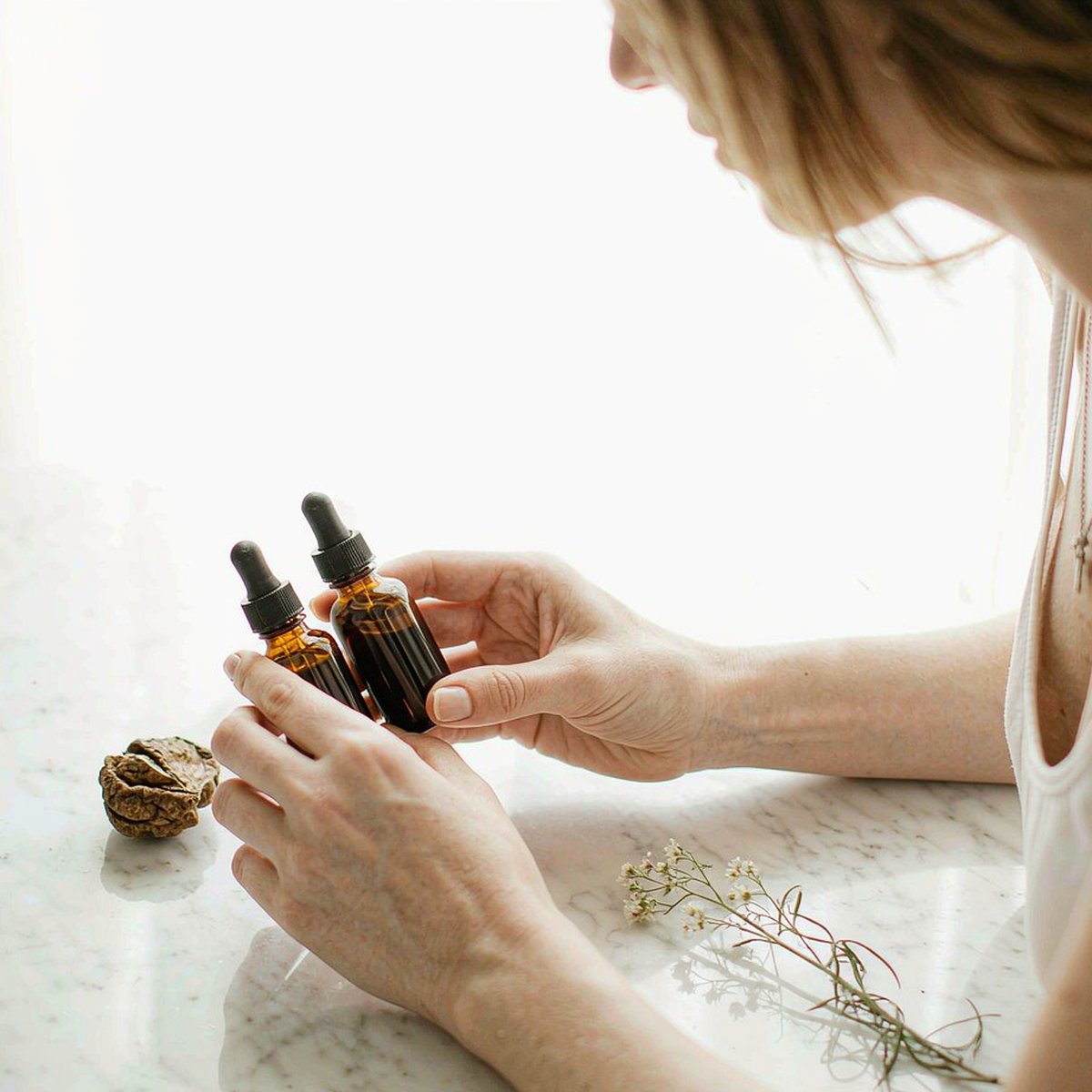 Caucasian mother with fair light skin compares two amber Black Walnut and Wormwood dropper bottles on a bright marble island