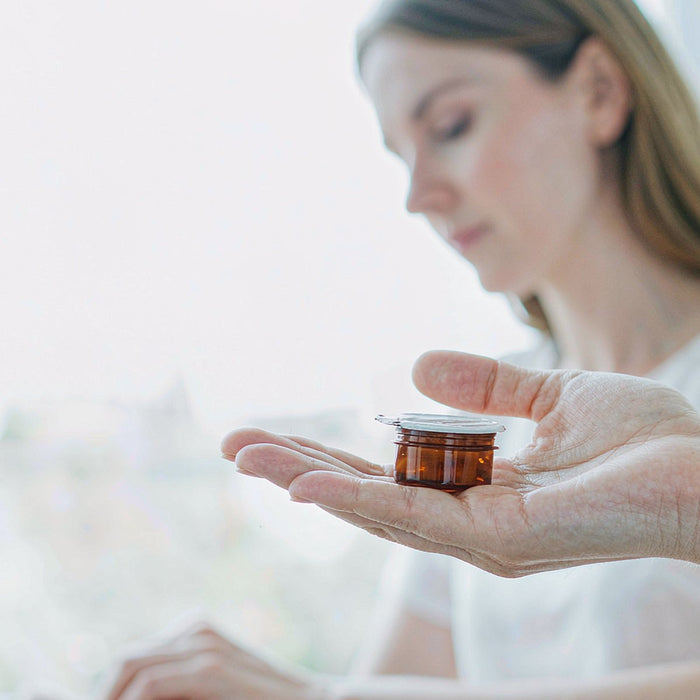Caucasian woman with fair light skin holding an amber supplement gummy jar in her open palm at a bright minimal office desk