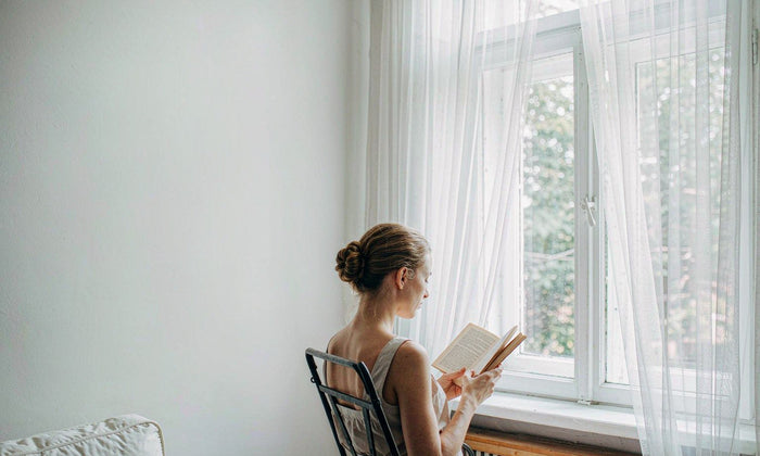 Western woman with light brown hair reading by a sunlit window, soft natural daylight, calm focus